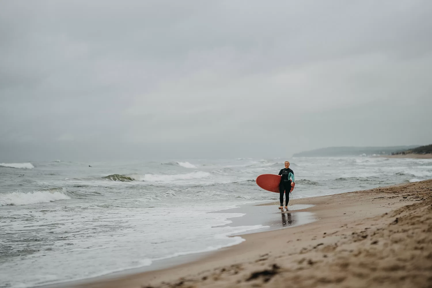 Surfer mit rotem Brett auf dem Weg ins Meer